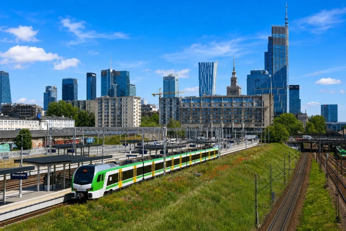 Зелений поїзд Koleje Mazowieckie на станції Варшава Головна на тлі міського небосхилу
