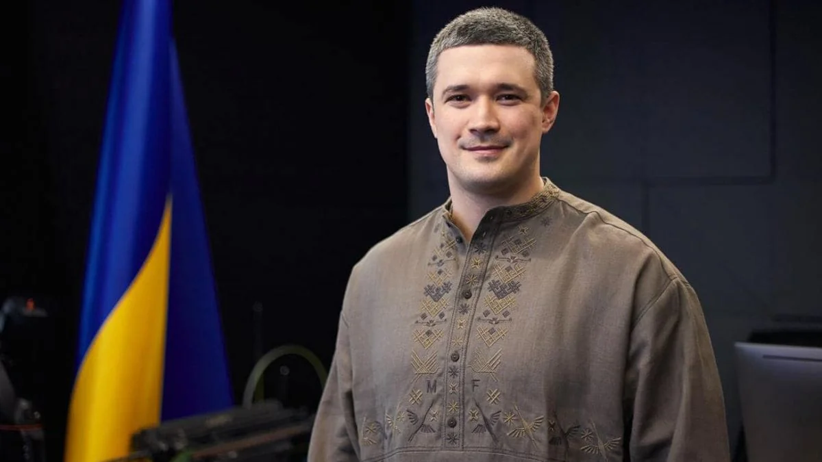Михайло Федоров у вишиванці стоїть біля українського прапора