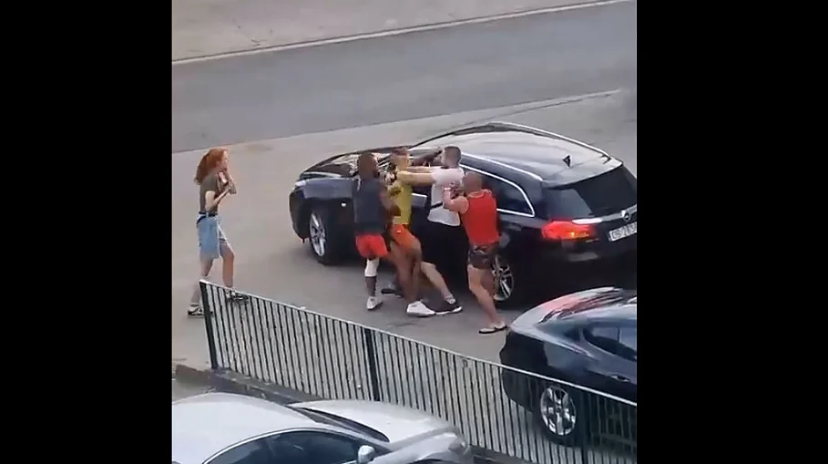 Чоловіки бються біля чорного автомобіля, рудоволоса жінка знімає на телефон