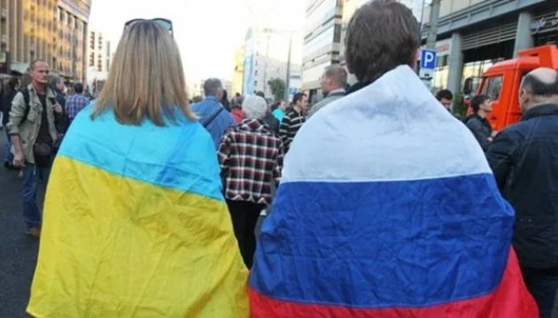 Люди з прапорами України та Росії стоять у натовпі на вулиці