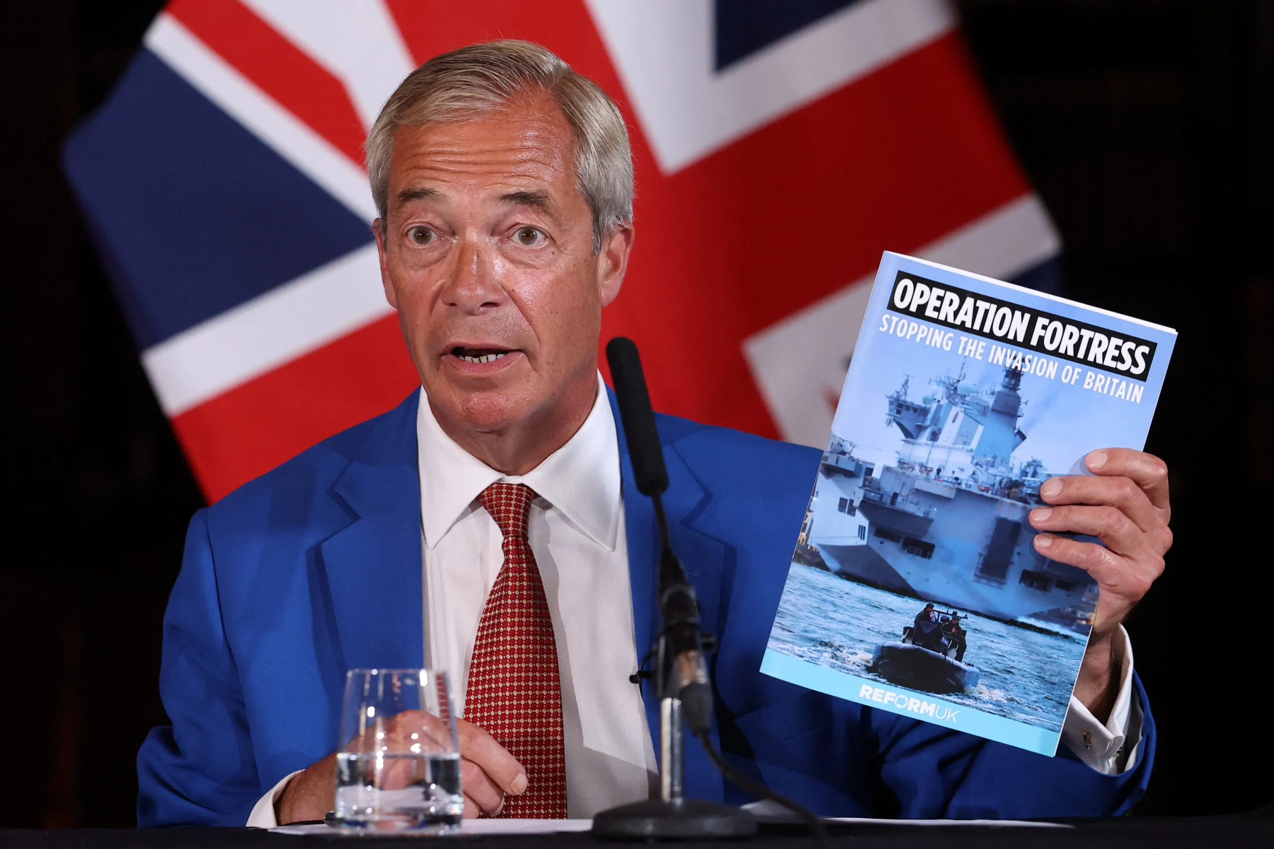 Найджел Фарадж тримає брошуру Operation Fortress на пресконференції Reform UK